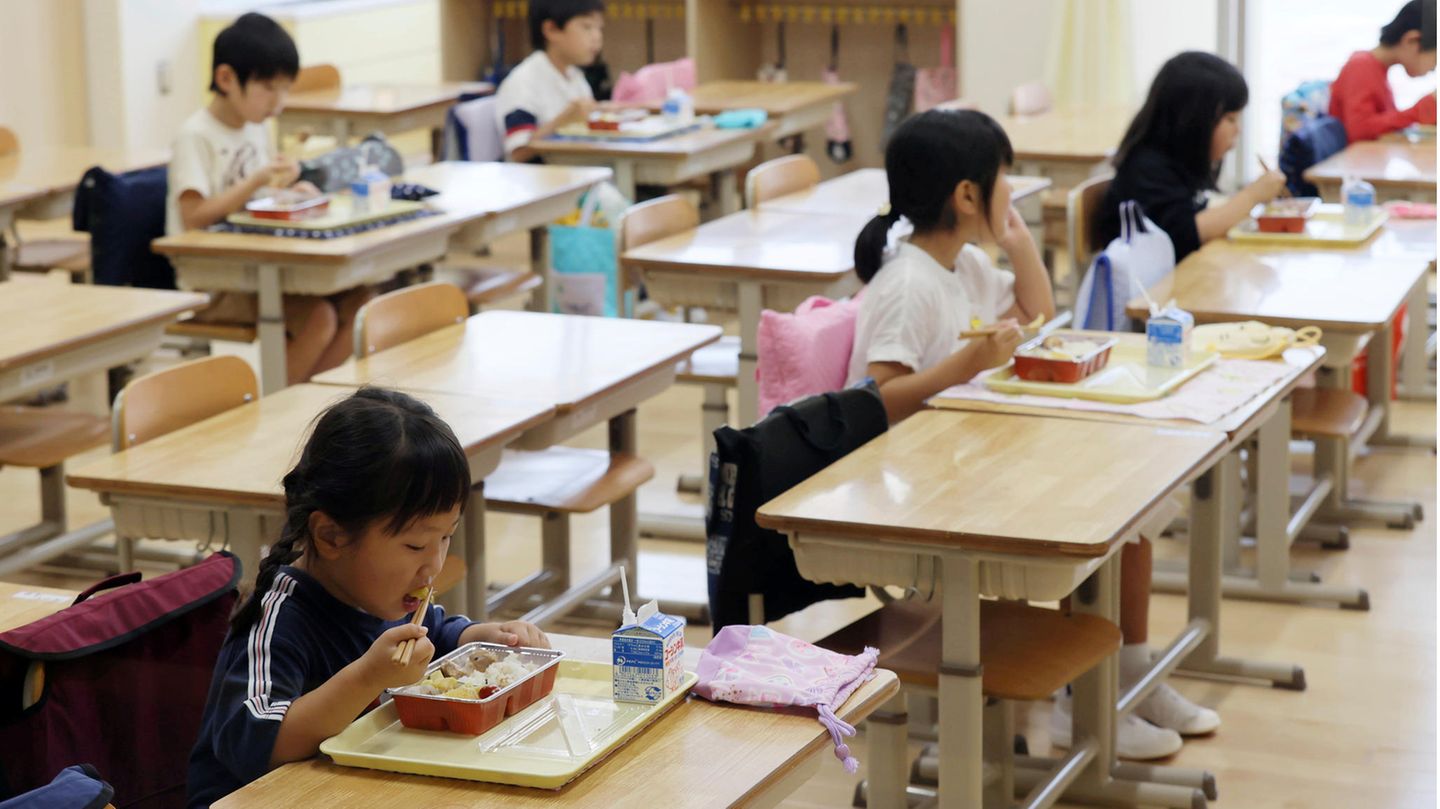 Aus der Vogelperspektive: Schüler in Japan essen an großen Tischen, durch Aufsteller sind sie voneinander getrennt