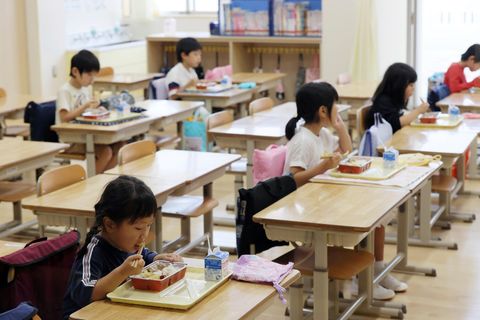 Aus der Vogelperspektive: Schüler in Japan essen an großen Tischen, durch Aufsteller sind sie voneinander getrennt
