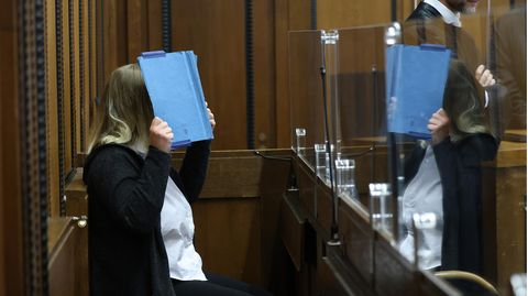 Die Angeklagte deckt im Landgericht ihr Gesicht mit einem blauen Ordner ab, vor ihr steht ihr Anwalt Felix Menke