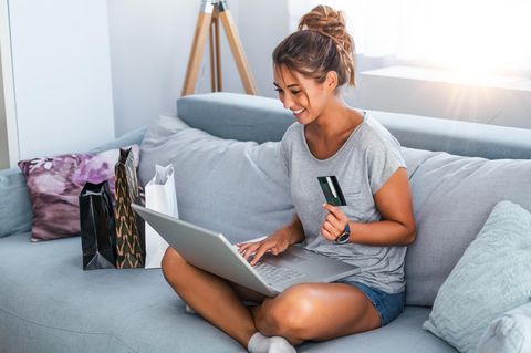 Eine Frau sitzt auf dem Sofa und kauf online ein.