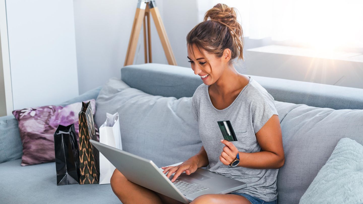 Eine Frau sitzt auf dem Sofa und kauf online ein.