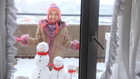 Ein Mädchen baut einen Schneemann auf dem verschneiten Balkon