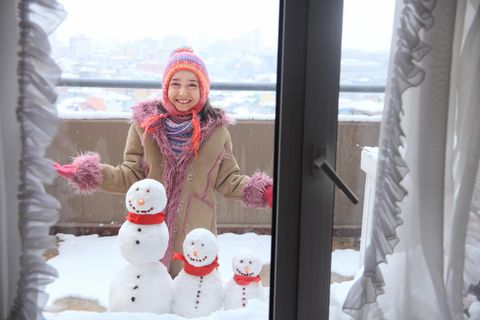 Ein Mädchen baut einen Schneemann auf dem verschneiten Balkon