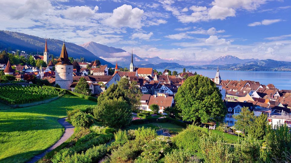 Der Zugersee in der Schweiz mit den Türmen der Altstadt von Zug davor und Bergen im Hintergrund