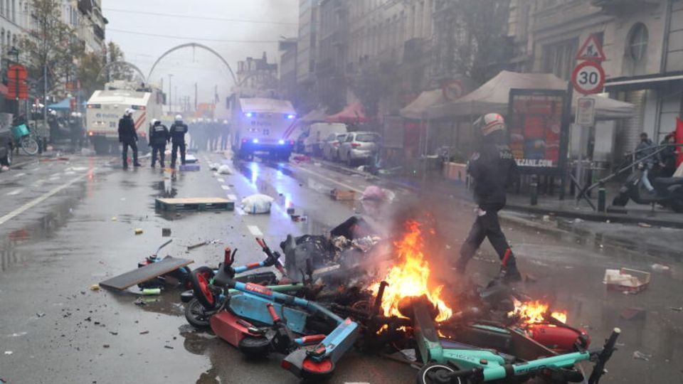 Polizisten gehen an Brand geratenem Müll und Leih-E-Scootern, die mitten auf der Straße in Brüssel liegen, vorbei