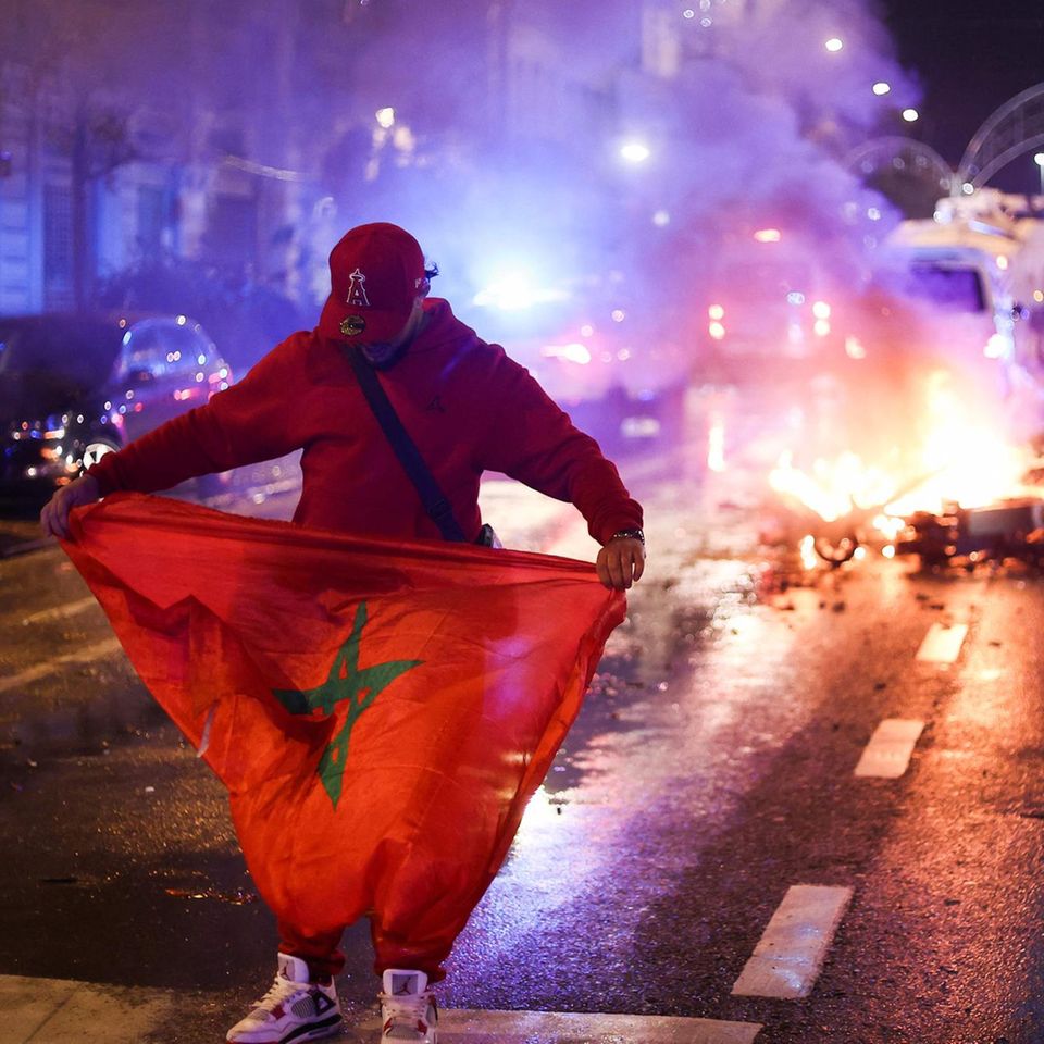 Brüssel, Belgien. Ein Mann steht mit auf einer Straße und breitet die marokkanische Flagge aus. Hinter ihm brennt ein E-Scooter, Feuerwehr Polizei haben sich bereits positioniert. Grund für dieses Chaos ist das WM-Spiel zwischen den belgischen und dem marokkanischen Nationalteams. Letztere gewannen, danach kam es zu Tumulten und Ausschreitungen, elf Personen wurden festgenommen.