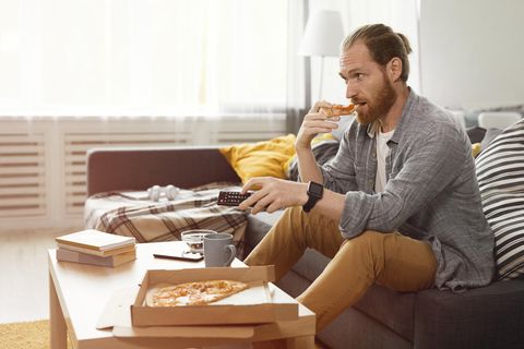 Mann isst Pizza auf der Couch