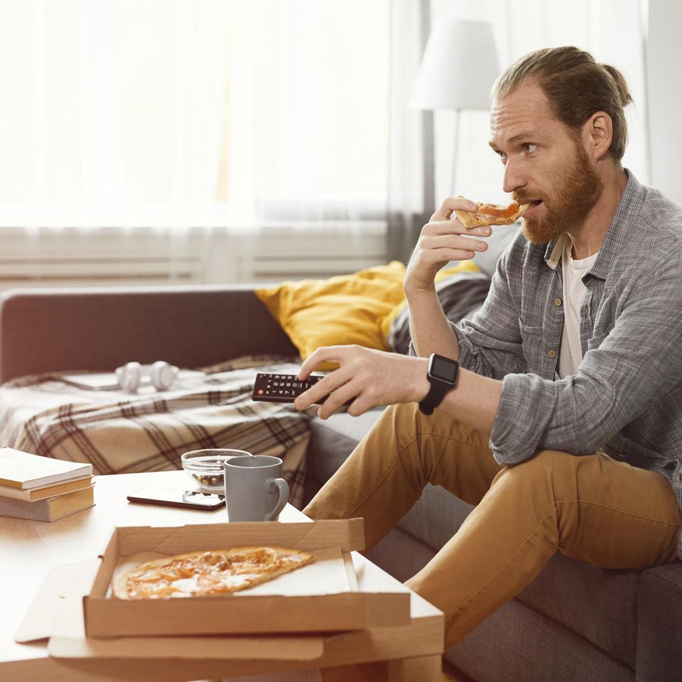 Mann isst Pizza auf der Couch