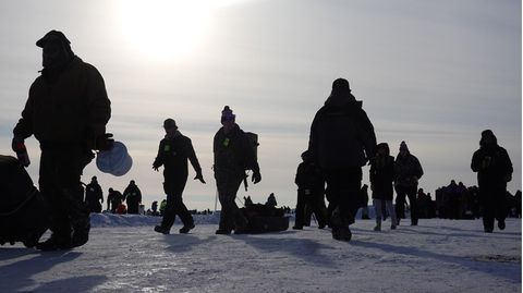 Im Gegenlicht sind nur die Konturen warm gekleideter Männer zu erkennen, die mit Angeln über eine Eisfläche gehen