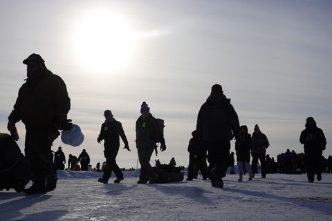 Im Gegenlicht sind nur die Konturen warm gekleideter Männer zu erkennen, die mit Angeln über eine Eisfläche gehen
