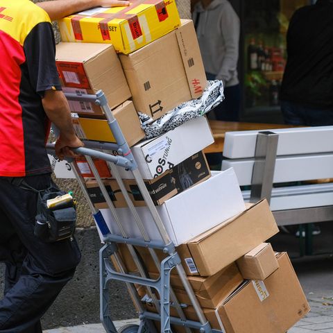 Paketbote schiebt auf Sackkarren viele Pakete vor sich her