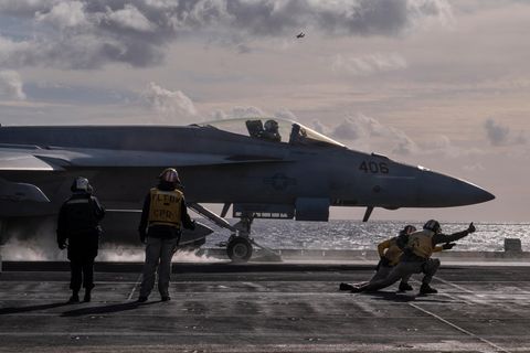 Kampfjet auf der USS George H.W. Bush kurz vor dem Start. Vordergrund geben Leute in der gelber Montur die letzten Befehle.