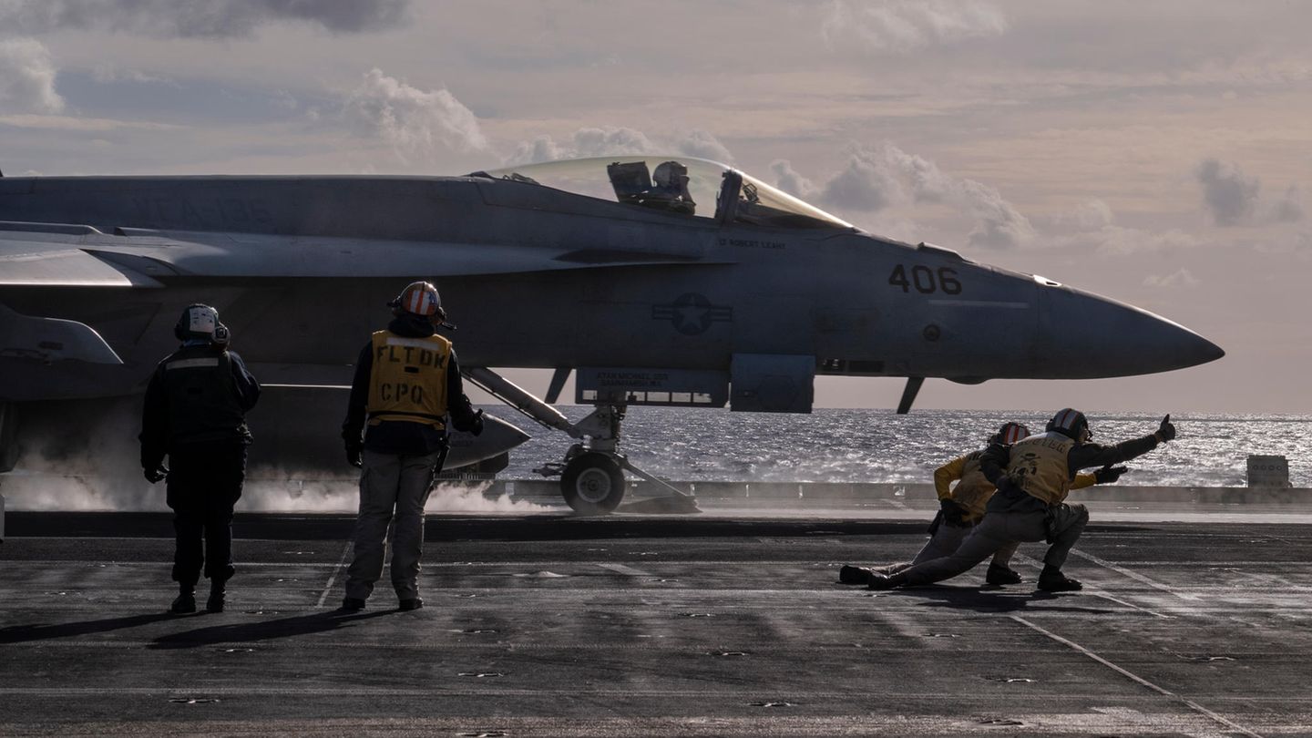 Kampfjet auf der USS George H.W. Bush kurz vor dem Start. Vordergrund geben Leute in der gelber Montur die letzten Befehle.