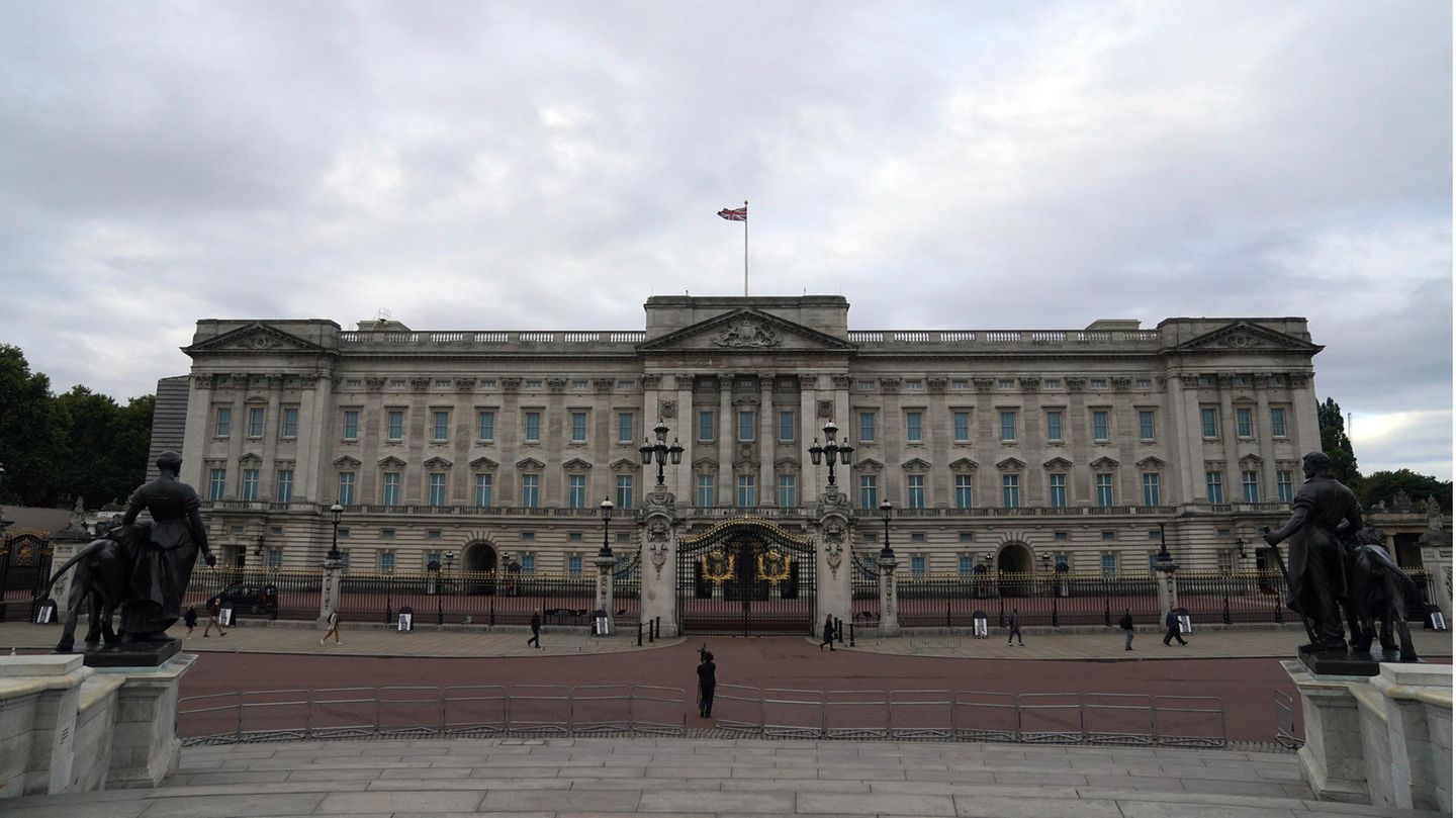 Unter einem dicht bewölkten Himmel steht ein lang gestrecktes historisches Gebäude, auf dem eine britische Flagge weht