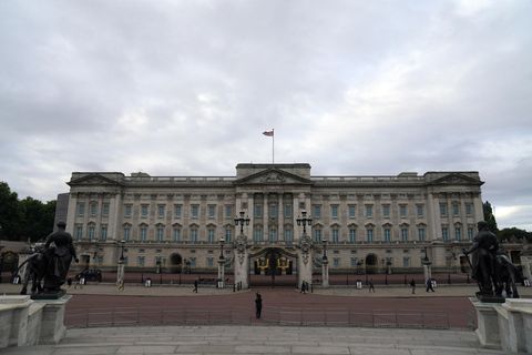 Unter einem dicht bewölkten Himmel steht ein lang gestrecktes historisches Gebäude, auf dem eine britische Flagge weht