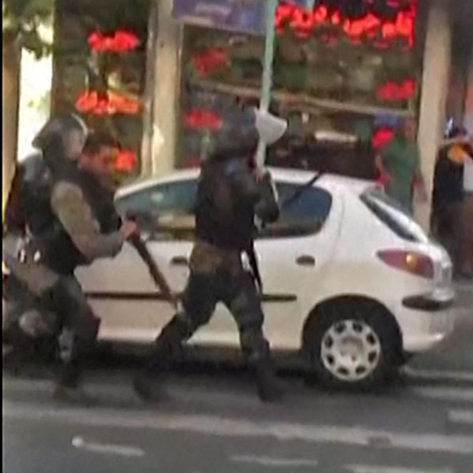 Behelmte Polizisten laufen auf einer Straße in Teheran an einem geparkten weißen Kleinwagen vorbei