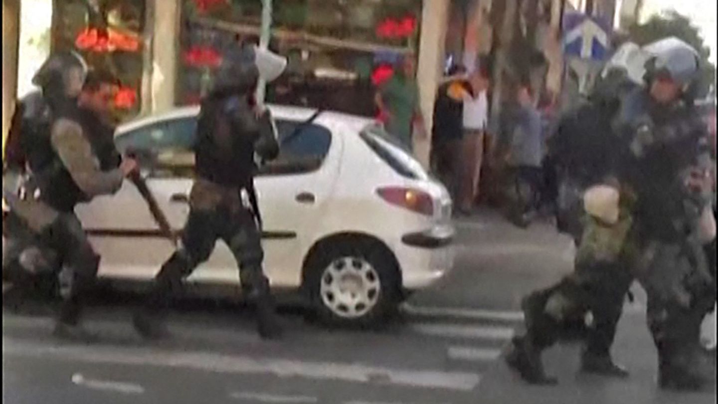 Behelmte Polizisten laufen auf einer Straße in Teheran an einem geparkten weißen Kleinwagen vorbei