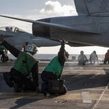 Zwei Personen in grün zeigen den Daumen nach oben. Im Hintergrund zwei Kampfjets.