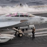 Kampfflugzeug an Deck, auf der Startbahn daneben raucht es vom Katapult.