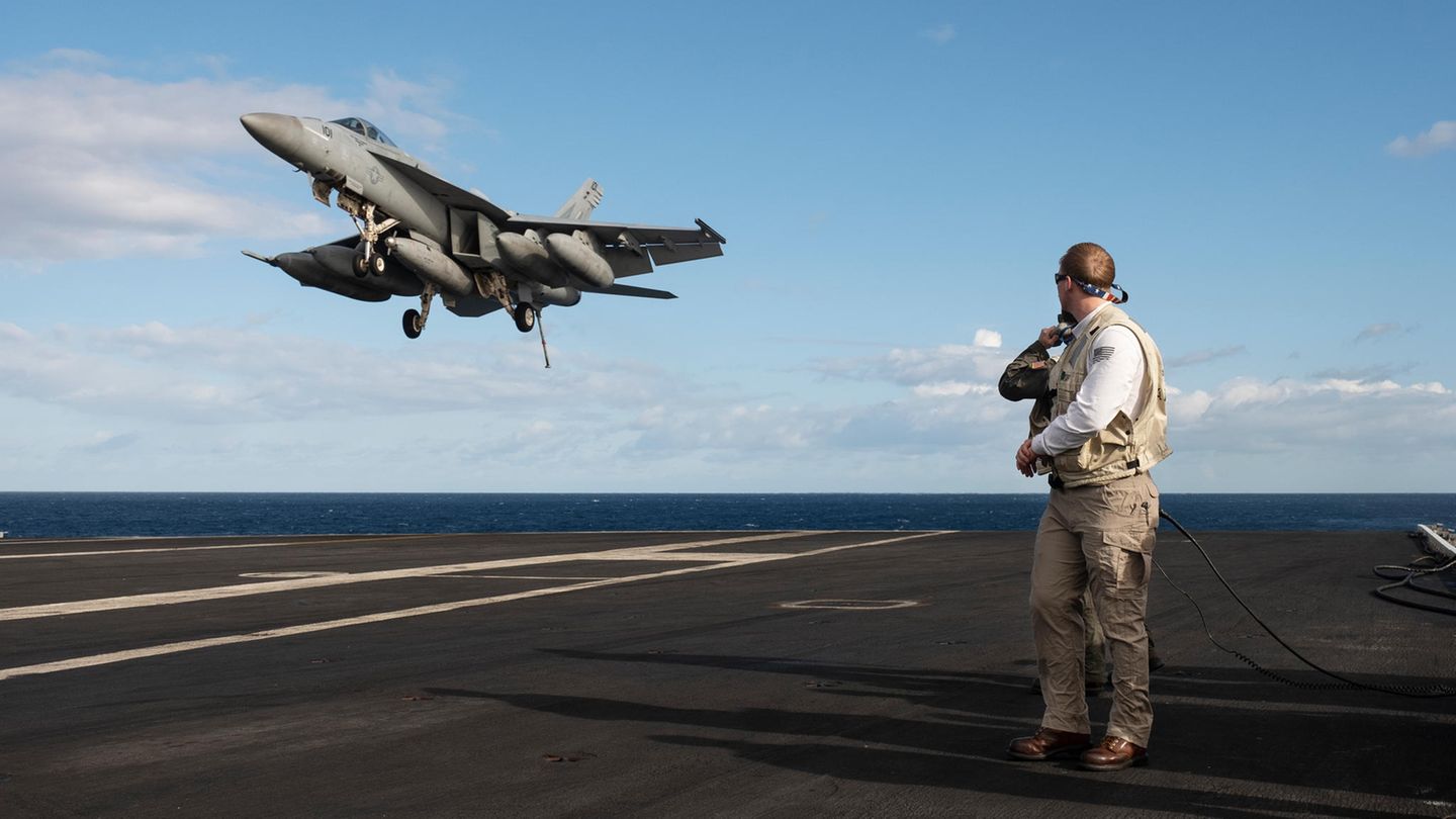 Kampfflugzeug landet auf der USS George H.W. Bush. Ein Mann schaut zum Flugzeug.