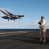 Kampfflugzeug landet auf der USS George H.W. Bush. Ein Mann schaut zum Flugzeug.