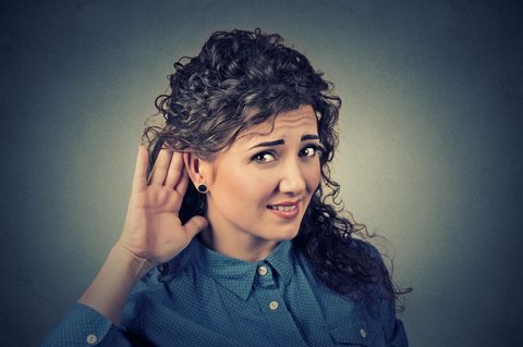 Eine Frau hält sich fragend eine Hand hinter ihr Ohr.