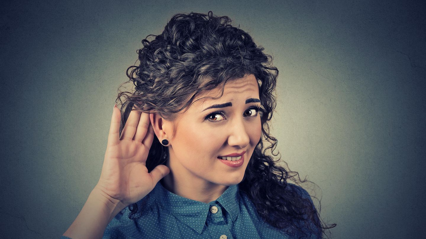 Eine Frau hält sich fragend eine Hand hinter ihr Ohr.