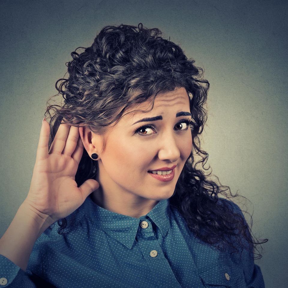 Eine Frau hält sich fragend eine Hand hinter ihr Ohr.