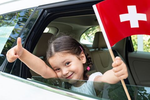 Ein Kind weht eine Schweiz-Fahne aus einem Autofenster heraus