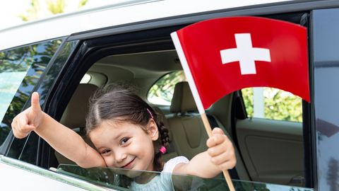 Ein Kind weht eine Schweiz-Fahne aus einem Autofenster heraus
