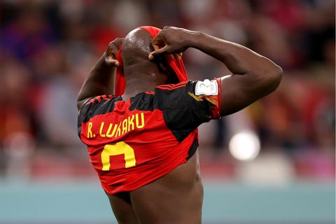 Ein schwarzer Fußballer verbirgt sein Gesicht in seinem rot-schwarzen Trikot mit gelbem "Lukaku"-Flock