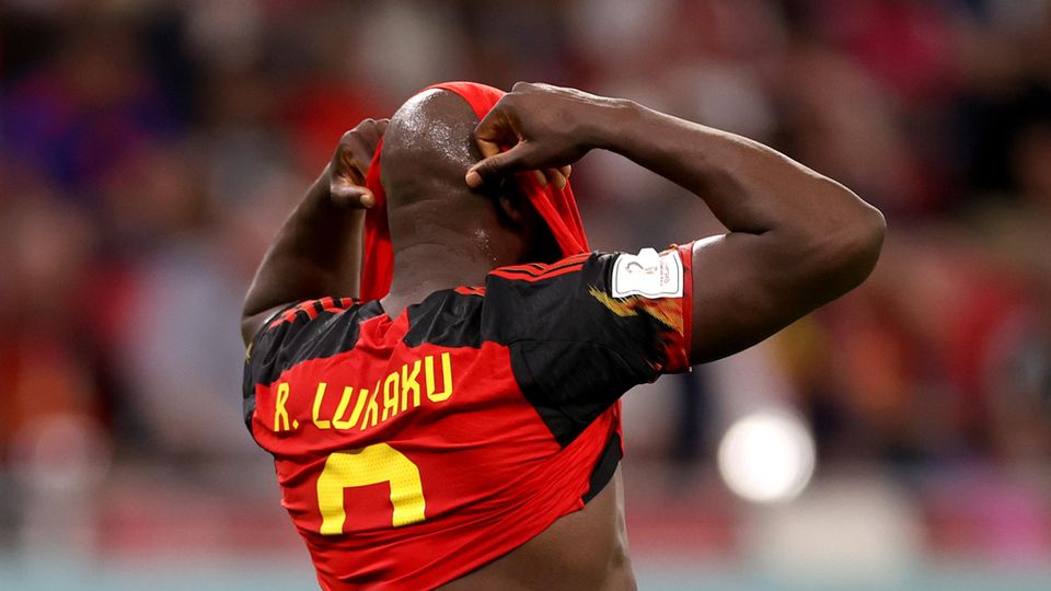 Ein schwarzer Fußballer verbirgt sein Gesicht in seinem rot-schwarzen Trikot mit gelbem "Lukaku"-Flock