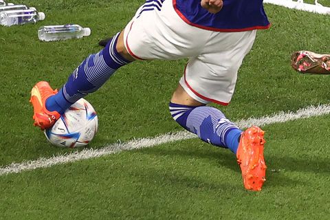 Ein asiatischer Fußballer in blauem Trikot und weißer Hose spielt mit dem linken Fuß einen Ball, der über die Torauslinie rollt