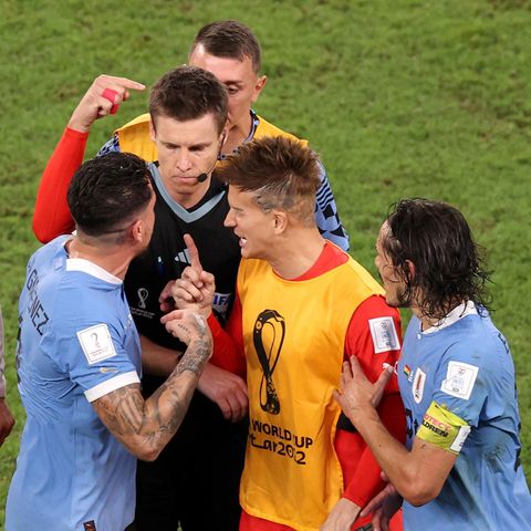 Um einen schwarz gekleideten Schiedsrichter hat sich eine Traube aus vier Fußball-Profis und einem Betreuer gebildet