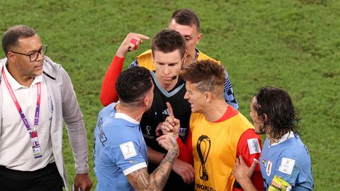 Um einen schwarz gekleideten Schiedsrichter hat sich eine Traube aus vier Fußball-Profis und einem Betreuer gebildet