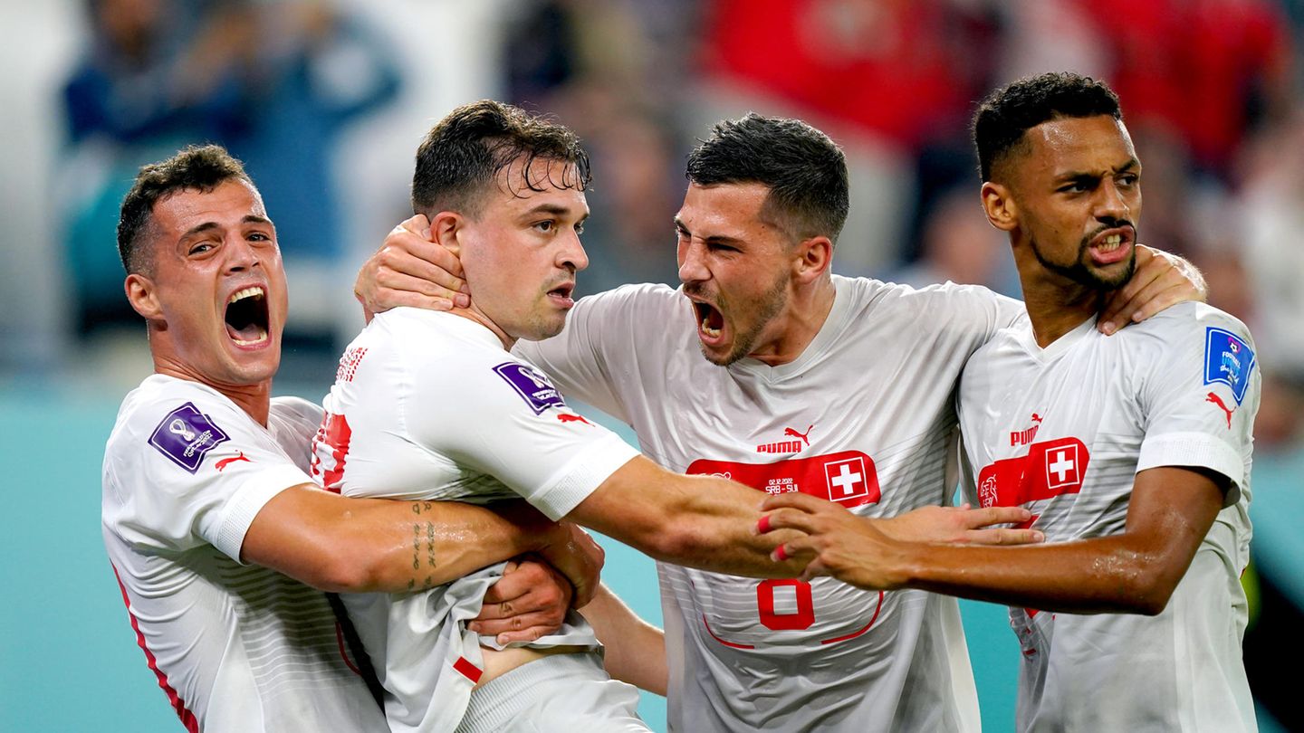 Vier weiße Fußball-Profis in weiß-roten Trikots umarmen sich beim Torjubel