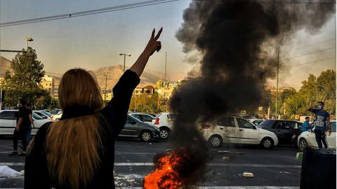 Iran: Eine Frau steht während einer Demonstration vor einem brennenden Autoreifen und zeigt das Victory-Zeichen