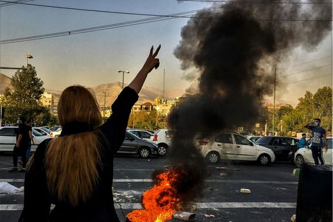 Iran: Eine Frau steht während einer Demonstration vor einem brennenden Autoreifen und zeigt das Victory-Zeichen