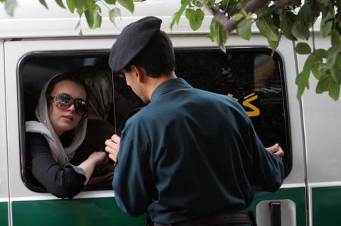 Ein iranischer Polizist spricht mit einer Frau, die in einem Polizeiauto sitzt