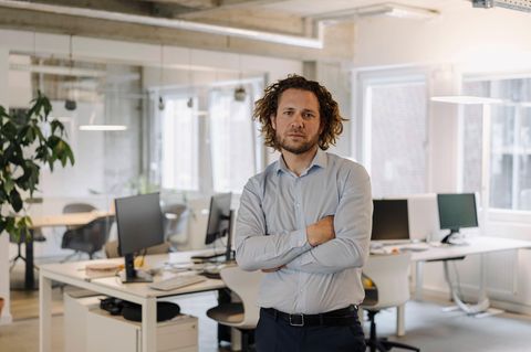 Ein Mann steht mit verschränkten Amren in seinem Büro und schaut arrogant