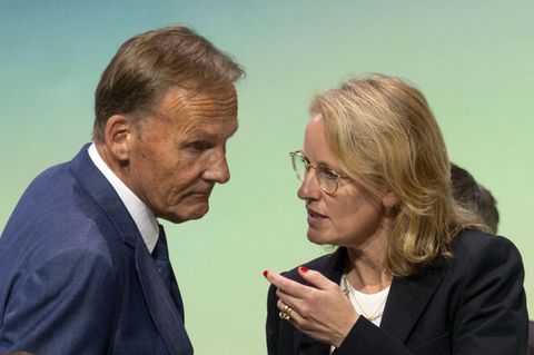 Ein älterer weißer Mann im blauen Anzug und mit graublondem Seitenscheitel beugt sich zu einer blonden Frau mit Brille herunter