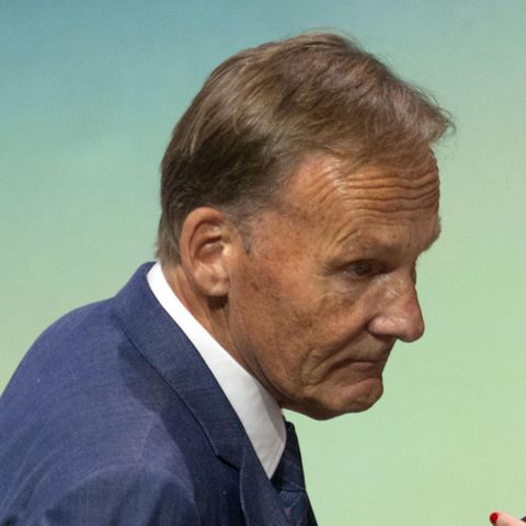 Ein älterer weißer Mann im blauen Anzug und mit graublondem Seitenscheitel beugt sich zu einer blonden Frau mit Brille herunter