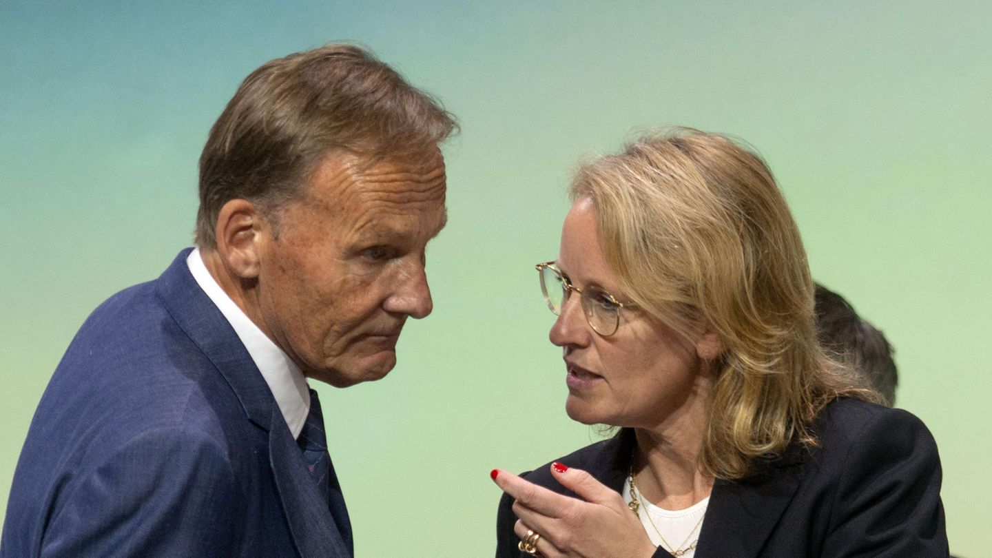Ein älterer weißer Mann im blauen Anzug und mit graublondem Seitenscheitel beugt sich zu einer blonden Frau mit Brille herunter