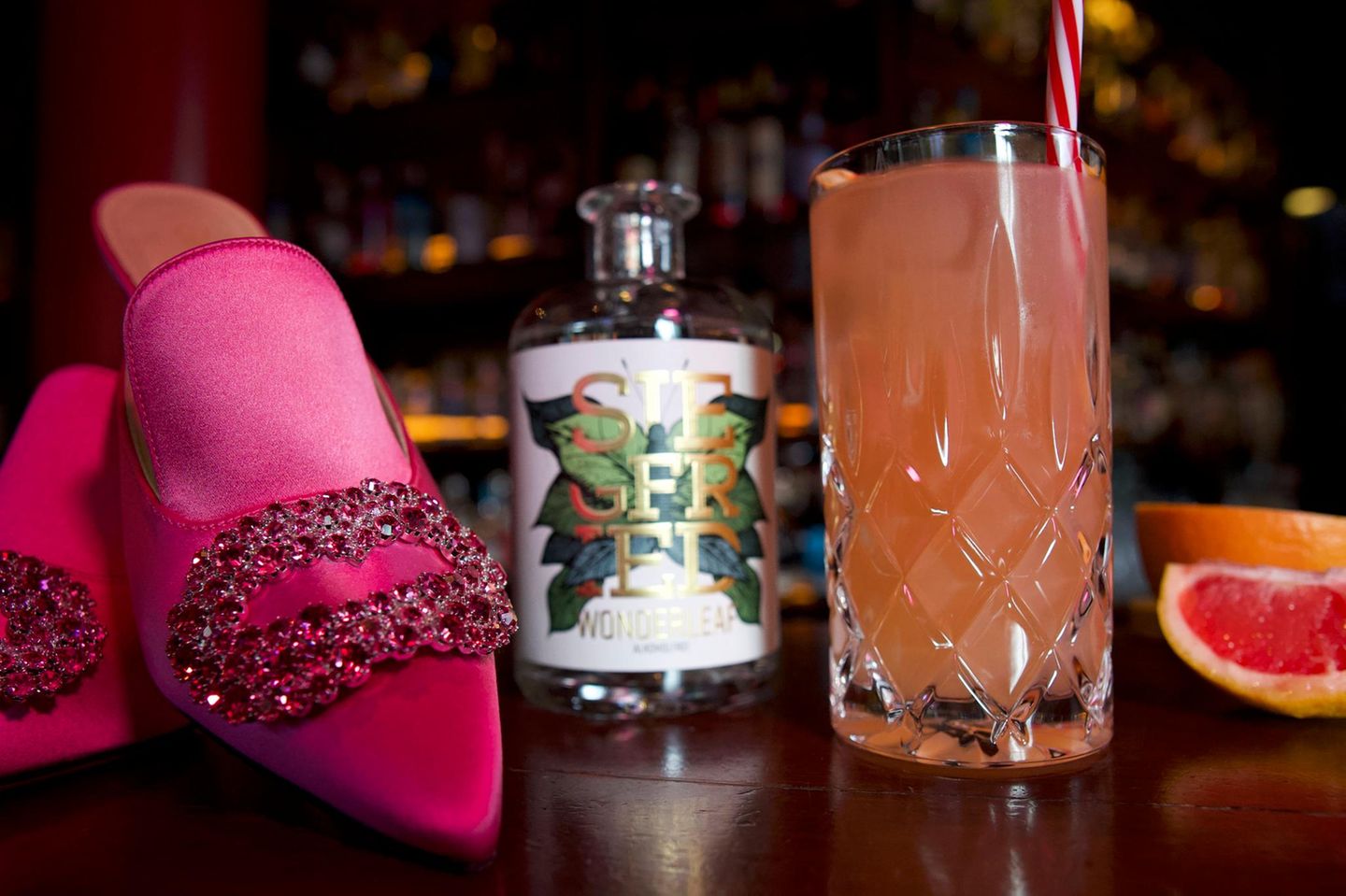 Eine Flasche alkoholfreier Gin, ein Glas Pinky Spicy und pinke Damenschuhe