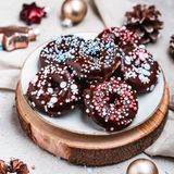 Weihnachtliche Mini-Donuts  Für ca. 14 Stück aus dem Mini-Donutmaker oder 6–8 Stück vom Donutblech  Für den Teig:  225 g Weizenmehl, 1 EL Backpulver, 65 g Rohrohrzucker, 1⁄2 TL Zimt, gemahlen, 125 g veganer Quark auf Mandelbasis, 160 ml Mandeldrink, 45 g Rapsöl zzgl. etwas mehr für die Form  Für die Glasur:  75 g Schokodrops, 50 g vegane Spekulatiuscreme vegane Streusel      Zubereitung:  Die Platten des Mini-Donutmakers bzw. das Donutblech mit etwas Rapsöl bepinseln. Das Gerät anschalten oder alternativ den Backofen auf 175 °C Ober-/Unterhitze vorheizen.  Für den Teig das Mehl und das Backpulver in eine große Schüssel sieben. Den Zucker und den Zimt hinzufügen. Den Quark, den Mandeldrink und das Rapsöl in die Schüssel geben und alles mit den Knethaken des Handrührgeräts vermengen.  Mithilfe von zwei kleinen Löffeln den Teig in den Donutmaker bzw. in das Donutblech füllen und goldbraun ausbacken. Die Donuts aus der Form lösen und abkühlen lassen.  Für die Glasur die Schokodrops und die Spekulatiuscreme auf einem heißen Wasserbad schmelzen. Die Donuts mit der Oberseite in die Glasur tauchen, abtropfen lassen und auf einem Teller platzieren. Mit den Streuseln dekorieren und trocknen lassen. Die Donuts sofort oder abgekühlt servieren.