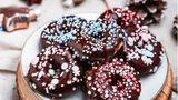 Weihnachtliche Mini-Donuts  Für ca. 14 Stück aus dem Mini-Donutmaker oder 6–8 Stück vom Donutblech  Für den Teig:  225 g Weizenmehl, 1 EL Backpulver, 65 g Rohrohrzucker, 1⁄2 TL Zimt, gemahlen, 125 g veganer Quark auf Mandelbasis, 160 ml Mandeldrink, 45 g Rapsöl zzgl. etwas mehr für die Form  Für die Glasur:  75 g Schokodrops, 50 g vegane Spekulatiuscreme vegane Streusel      Zubereitung:  Die Platten des Mini-Donutmakers bzw. das Donutblech mit etwas Rapsöl bepinseln. Das Gerät anschalten oder alternativ den Backofen auf 175 °C Ober-/Unterhitze vorheizen.  Für den Teig das Mehl und das Backpulver in eine große Schüssel sieben. Den Zucker und den Zimt hinzufügen. Den Quark, den Mandeldrink und das Rapsöl in die Schüssel geben und alles mit den Knethaken des Handrührgeräts vermengen.  Mithilfe von zwei kleinen Löffeln den Teig in den Donutmaker bzw. in das Donutblech füllen und goldbraun ausbacken. Die Donuts aus der Form lösen und abkühlen lassen.  Für die Glasur die Schokodrops und die Spekulatiuscreme auf einem heißen Wasserbad schmelzen. Die Donuts mit der Oberseite in die Glasur tauchen, abtropfen lassen und auf einem Teller platzieren. Mit den Streuseln dekorieren und trocknen lassen. Die Donuts sofort oder abgekühlt servieren.