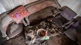Möbel und Geschirr liegen mit Asche bedeckt in einem Wohnzimmer im Dorf Kajar Kuning