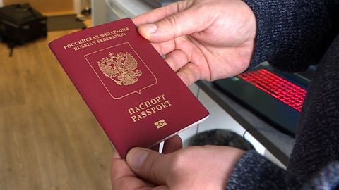 Ein Mann hält mit beiden Händen einen roten Reisepass mit kyrillischer Schrift und "Passport"-Aufdruck