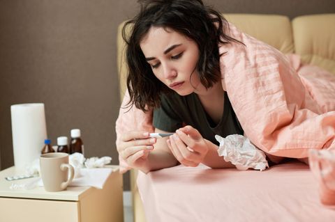 Frau misst Fieber und liegt mit Grippe im Bett