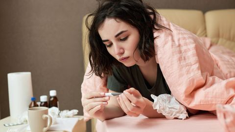 Frau misst Fieber und liegt mit Grippe im Bett